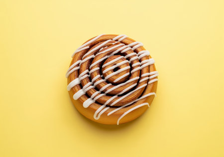 Delicious cinnamon roll topped with sweet white icing, presented on a vibrant pastel yellow background. freshly baked pastry, perfect for breakfast or dessert.の素材