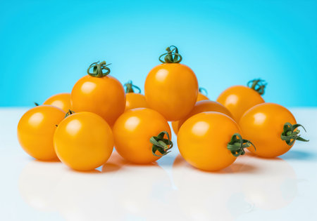 Fresh bright yellow grape tomatoes with green stems, neatly clustered on a reflective white surface against a vibrant blue background. healthy, organic, and ripe produce.の素材