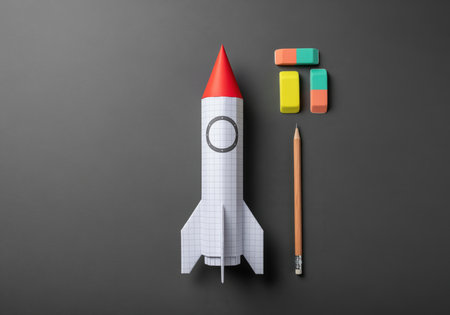 Graph paper rocket, wooden pencil, and colorful erasers arranged on a dark gray surface. represents education, startup, creativity, and project launch.の素材