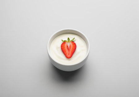 Creamy vanilla yogurt in a small white ceramic bowl, garnished with a vibrant red strawberry half. healthy, fresh, and delicious dairy snack or breakfast option.の素材