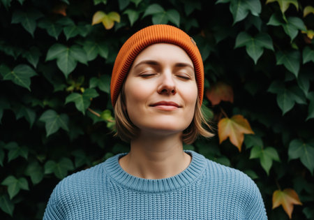 A serene woman with closed eyes and a gentle smile, wearing an orange beanie and blue sweater, embodies tranquility and peaceful reflection. ideal for themes of mindfulness, relaxation, and well being.の素材