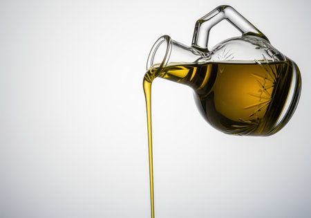 A smooth, steady stream of golden olive oil pours from a decorative clear glass carafe, ideal for culinary themes, healthy eating, and cooking concepts.の素材