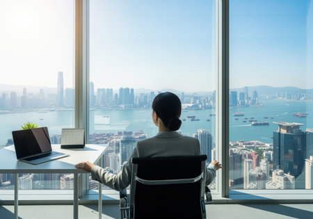 An asian businesswoman sits in a modern office, looking out a large window at a sprawling city skyline and busy harbor. a laptop and plant are on her desk, conveying success and contemplation.の素材