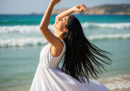 A serene woman with long flowing black hair and a white dress dances on a sunny beach. she is enjoying the warmth and freedom of a beautiful summer day.の素材