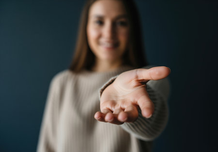 A young woman extends her open hand towards the viewer, symbolizing an offer, request, or connection. this gesture can represent giving, receiving, or inviting assistance.の素材