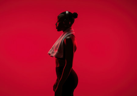 A powerful silhouette of an african female athlete in profile, wearing headphones and a towel, conveying strength and readiness for training.の素材