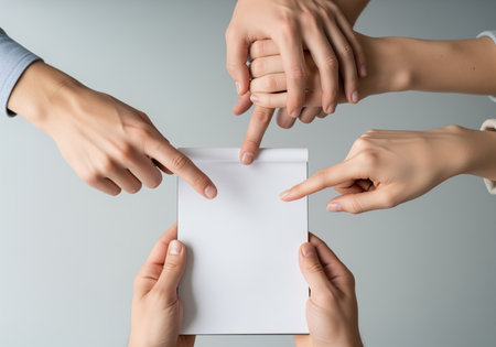 A close up view of several hands pointing at a blank white notepad, held by two other hands. this image represents teamwork, brainstorming, and shared decision making, ideal for business concepts.の素材