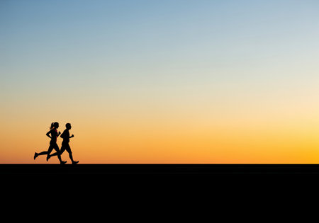 A striking silhouette of a man and woman running side by side, captured against a beautiful gradient sunset. ideal for themes of fitness, partnership, and outdoor activity.の素材