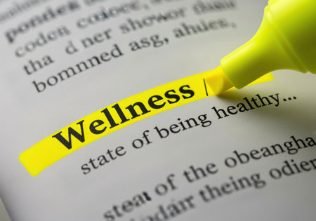 The word wellness is highlighted in yellow in a dictionary, with its definition tate of being healthy visible. this image represents health, well being, and personal care.の素材