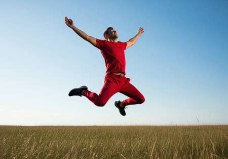 A vibrant shot of a man in red sportswear mid air, arms outstretched, celebrating freedom and success. this dynamic image conveys energy and happiness.の素材