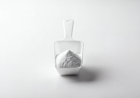 White powdered substance mounded in a clean, white plastic measuring scoop, centrally placed on a bright, minimalist background with soft shadows, ready for use.の素材