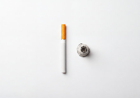 Unlit cigarette presented alongside a pile of cigarette ash on a clean white surface, symbolizing the cycle of smoking, addiction, health problems, and the journey toward quitting or cessation.の素材