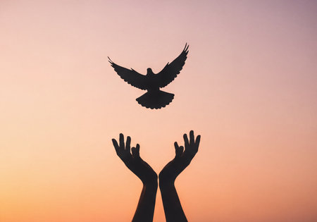 Silhouette of human hands reaching up towards a dove in flight, against a vibrant gradient sky at sunset. Represents concepts of peace, freedom, hope, letting go, and spirituality.の素材