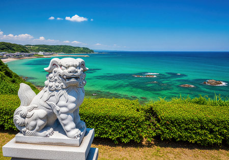 Traditional Japanese Shisa guardian lion statue positioned on a green hillside, offering a panoramic view of a beautiful tropical beach, clear turquoise sea, and lush coastal landscape in Okinawa, Japan.の素材
