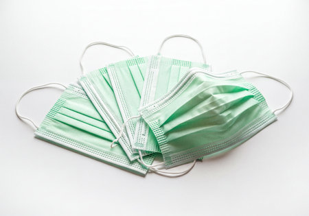 Numerous light green disposable medical surgical face masks, offering protection against airborne particles, viruses, bacteria, and pollution, arranged on a clean white background.の素材