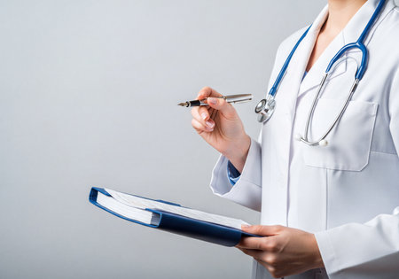 Medical professional in a white lab coat, holding a pen and a blue clipboard with documents. A stethoscope is draped around the neck, signifying healthcare, medical procedures, and hospital settings.の素材