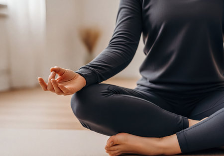 Person in comfortable activewear sitting cross-legged on a yoga mat, hands in meditation mudra, fostering relaxation, mindfulness, balance, and inner peace.の素材