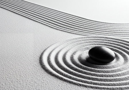 Black smooth stone placed amidst meticulously raked white sand in a Japanese zen garden, creating patterns of calm and tranquility with concentric circles and linear paths in grayscale.の素材