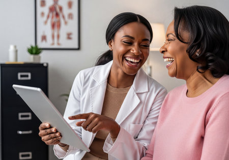 A cheerful black female physician and her patient share a laugh while reviewing information on a digital tablet during a medical consultation. depicts positive patient care.の素材