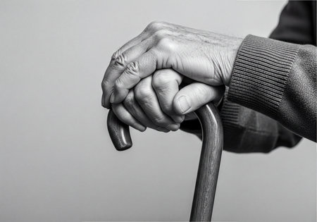 Elderly man&#39;s hands, visibly aged, clasped firmly around the polished handle of a wooden walking stick. The black and white image emphasizes texture and highlights the theme of aging, support, and care, suggesting stability and assistance.の素材