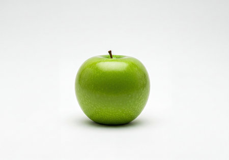 A single fresh green apple with a brown stem, glossy and vibrant, standing centered on a clean white studio background. Represents health, nutrition, freshness, and organic food.の素材