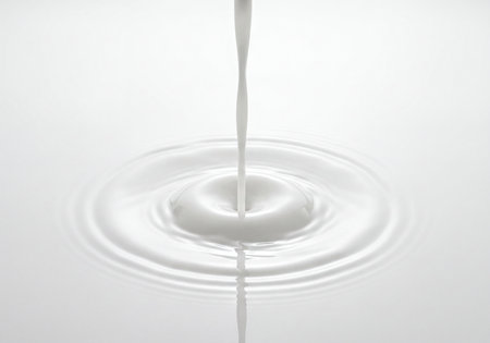 Smooth white liquid stream gently pours onto a calm surface, causing concentric ripples to spread out. Captures concepts of purity, freshness, flow, and smooth texture for food, cosmetic, and abstract designs.の素材