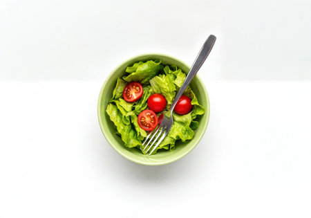 Overhead view of a vibrant green salad with fresh lettuce and halved cherry tomatoes served in a light green bowl with a fork. ideal for promoting healthy eating and balanced diets.の素材