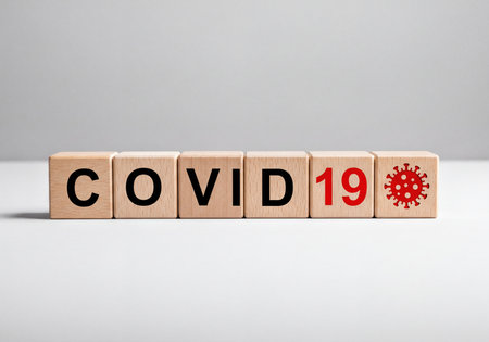 Wooden blocks arranged to spell COVID 19, with a red virus icon on the last block, symbolizing the global coronavirus pandemic and health crisis.の素材