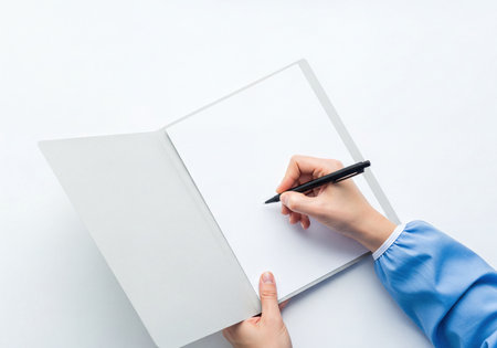 Female hand holding a black pen and writing on a blank white sheet of paper inside an open gray folder. A clean shot with abundant copy space for any text.の素材