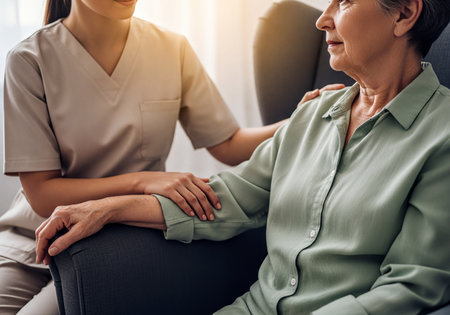 Compassionate caregiver gently supporting an elderly woman seated in an armchair. The scene captures a genuine moment of care, empathy, and professional assistance, highlighting well-being and connection.の素材