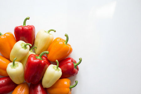 Fresh red orange and white bell peppers with water drops are clustered on a white surface with ample negative space for text placement and design layout.の素材