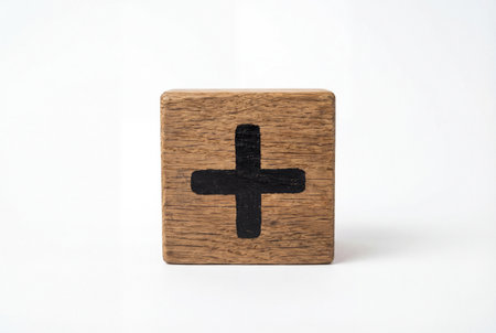 A square wooden block featuring a bold black plus symbol sits isolated on a clean white background to symbolize addition positivity and mathematical sums.の素材