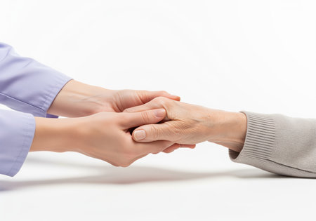 A young caregiver or nurse wearing a light purple uniform gently holds the wrinkled hand of an elderly woman patient, symbolizing support, trust, compassion, and professional healthcare assistance on a clean white background.の素材