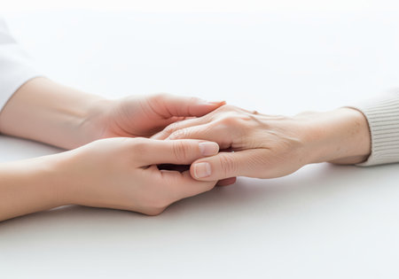 A close up shot of a younger person hand gently holding the hand of an elderly individual, symbolizing care, compassion, and support for aging and healthcare services.の素材