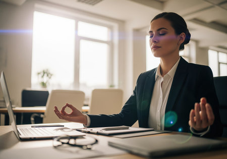 Professional woman in a suit takes a moment for peaceful meditation at her workplace, finding balance and reducing stress during a busy workday. this image represents corporate wellness and mental health initiatives.の素材