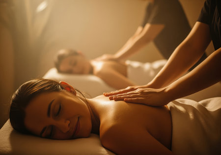 Two women receive simultaneous back massages in a dimly lit, luxurious spa environment. the warm light and soft focus emphasize relaxation, wellness, and therapeutic treatment.の素材