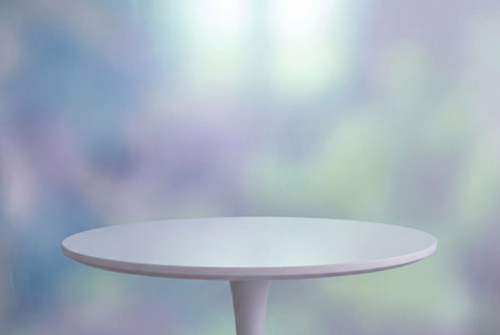 An empty white round table stands prominently against a soft defocused backdrop featuring abstract blends of blue purple and light green colors for product placement.の素材