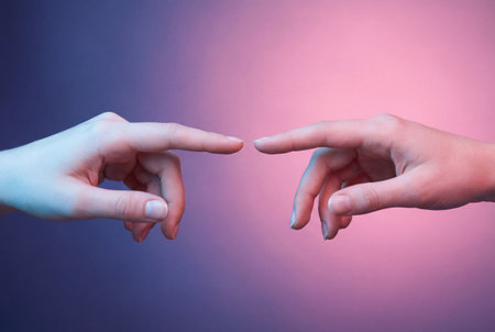Two human hands extend from opposite sides towards the center with index fingers almost touching against a purple and blue gradient studio background.の素材