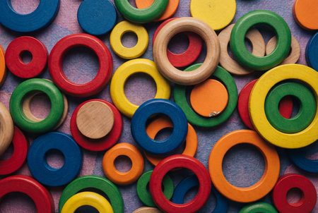 Top down view of assorted colorful wooden toy rings and solid disks scattered randomly across a textured blue and purple surface to create a vibrant abstract geometric pattern.の素材
