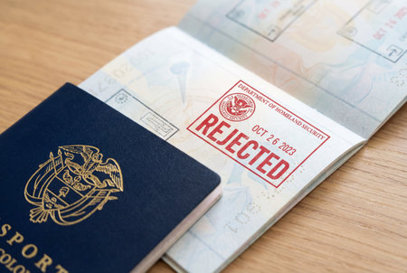 Close up of an open colombian passport on a wooden table showing a bright red ink stamp stating rejected issued by the US department of homeland security for entry denial.の素材