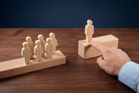 A male hand selects a single wooden figure standing on a higher block separate from a group on a lower level to illustrate leadership selection promotion and business hierarchy.の素材