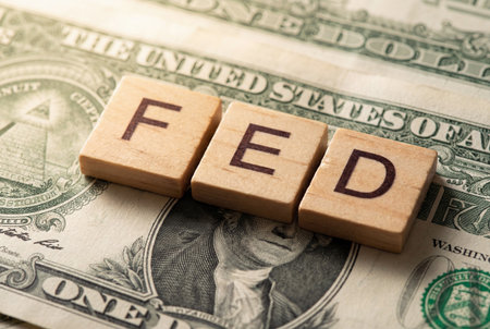 Three wooden letter tiles spelling FED rest on a US one dollar bill representing the federal reserve system and its significant influence on american financial markets and monetary policy.の素材