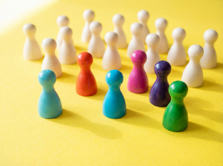 A diverse group of colorful wooden game pieces stands in the foreground representing leaders while a large crowd of white pawns gathers behind them on a bright yellow surface.の素材