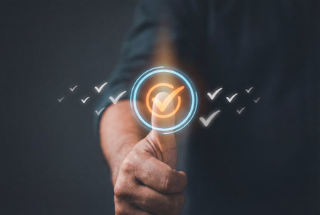 A male hand showing a thumbs up gesture with a glowing digital checkmark icon floating above the thumb to symbolize successful completion and positive feedback or approval on a dark background.の素材