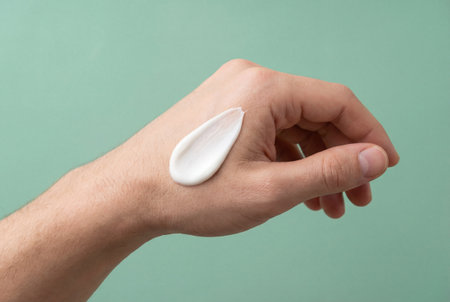 Close-up shot of a white creamy cosmetic swatch on the back of a man's fair-skinned hand, highlighting product texture and application for beauty and skincare marketing purposesの素材