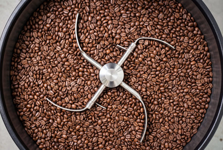 Abundance of freshly roasted rich brown coffee beans filling the polished black matte cooling drum in a commercial roasting machine with central metal agitator for even distribution during cooling processの素材