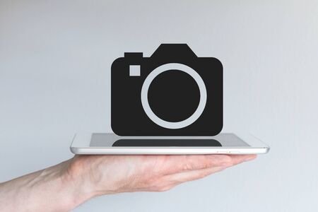 Concept of smartphone or tablet as replacement for digital camera DSLR. Male hand holding tablet or smartphone with camera symbol.の写真素材