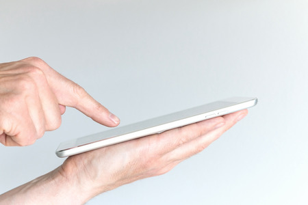 Male hand holding modern tablet or large smart phone. Other hand pointing at screen of mobile device with one finger. Concept of mobile computing and information technology.の写真素材