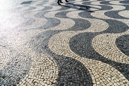 Walking people casting a long shadow on pavementの写真素材