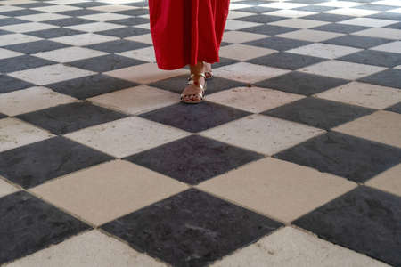 Close up of a woman in red dress and elegant sandals walking on a checkered marble black and white floorの写真素材